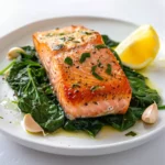 baked salmon with spinach served on a plate with garlic and lemon